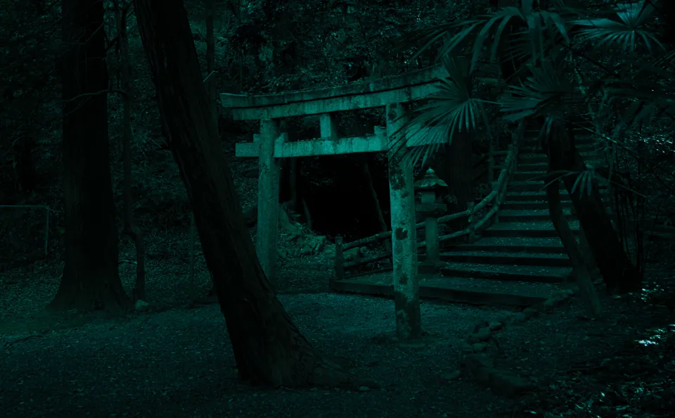A weathered stone torii gate stands on steps leading into a dark forest, cast in a cool teal tone, palm fronds overhanging the path.